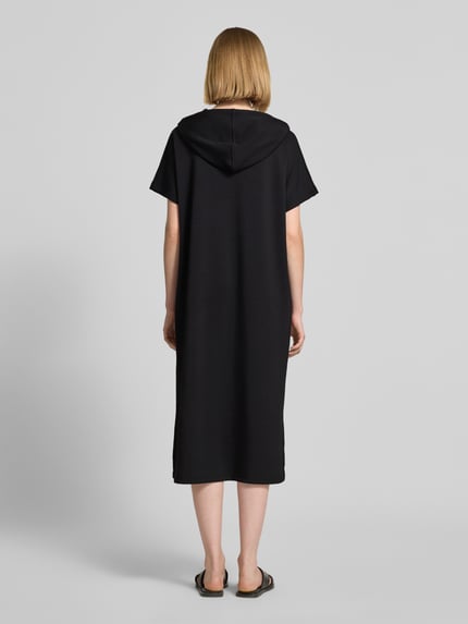 Frauenmodel trägt Sweatkleid mit Kapuze von Soyaconcept in Schwarz, Material-Mix mit Modal-Anteil, Gerader-Schnitt, Midikleid, Label-Print, Ganzkörperansicht Rückansicht.