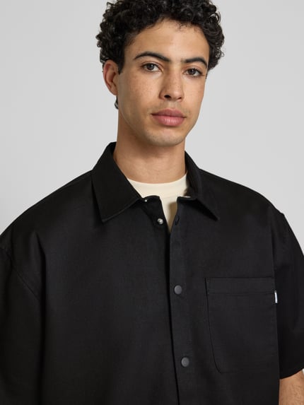 Männermodel trägt Relaxed Fit Freizeithemd mit Brusttasche von REVIEW, Material-Mix, Kentkragen, Knopfleiste, 1/2-Arm, Nahaufnahme Oberkörper.