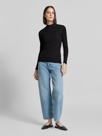 Vrouwenmodel draagt Slim Fit gebreide pullover uit puur katoen model 'ALAANIA' van Armedangels, look: effen, langemouw, hooggesloten, labelpatch, gestikt logo, materiaalverwerking: knitwear, kleur zwart, ganzecorpsaanzicht van voren.