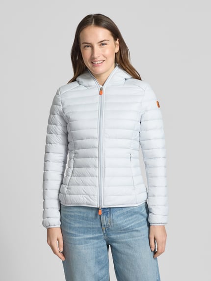 Frauenmodel trägt Slim Fit Steppjacke im Zweiwegereißverschluss Modell 'Daisy' von SAVE THE DUCK in hellblau, gesteppt, mit Kapuze und Reißverschlusstaschen, Ganzkörperansicht von vorne.