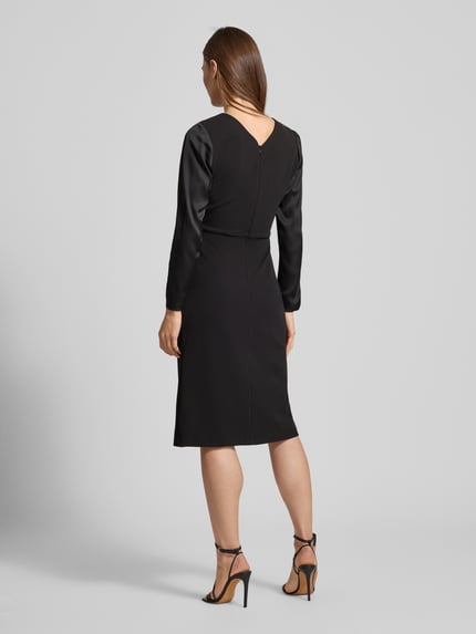 Frauenmodel trägt Cocktailkleid mit Raffungen von Rinascimento in Schwarz, Material-Mix mit Stretch-Anteil, taillierter Schnitt, U-Ausschnitt, Gehschlitz und Nahtreißverschluss, Ganzkörperansicht Rückansicht.