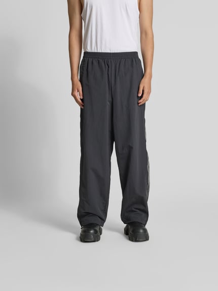 Männermodel trägt Sweatpants mit elastischem Bund von VETEMENTS in Schwarz, Relaxed-Fit, Eingrifftaschen, Beinabschlüsse mit Tunnelzug, Wide Leg, Ganzkörperansicht von vorne.