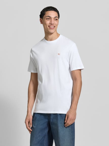 Männermodel trägt T-Shirt mit Label-Patch Modell 'BADGE' im 2er-Pack von Calvin Klein Jeans, reine Baumwolle, weiß, Ganzkörperansicht von vorne.