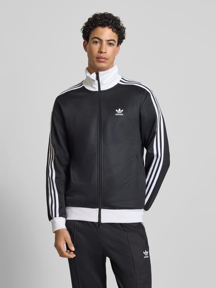 Mannelijk model draagt Sweatjacke mit Reißverschluss van adidas Originals in zwart-wit, losvallende pasvorm, ribboorden, staande kraag, labelstiksel, ritszakken, katoenmix. Ganzkörperansicht van voren.