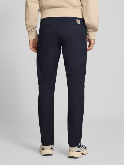 Männermodel trägt Skinny Fit Hose aus Baumwoll-Mix Modell 'SID' von Carhartt Work In Progress in Dunkelblau, Ganzkörperansicht Rückansicht. Bundweite 45 cm, Innenbeinlänge 79 cm, Seiten- und Gesäßtaschen.