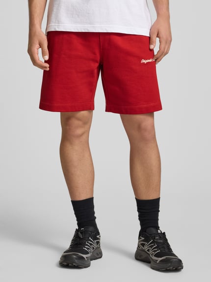 Männermodel trägt Shorts mit Label-Stitching Modell 'KARL' von Jack & Jones aus Baumwoll-Mix, Relaxed-Fit, rote Farbe, Ganzkörperansicht von vorne.