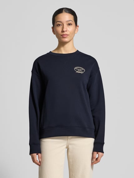 Modelka kobieca nosi Sweatshirt mit Label-Stitching und Rundhalsausschnitt od Gant, bawełna, krój loose fit, granatowy, ściągacze, widok od przodu, ujęcie całej sylwetki.