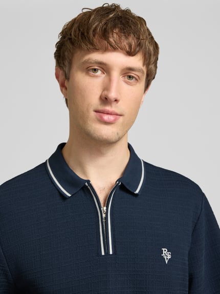 Männermodel trägt Regular Fit Poloshirt mit Reißverschluss und Label-Stitching von REVIEW, dunkelblau mit Strukturmuster, Nahaufnahme Oberkörper.