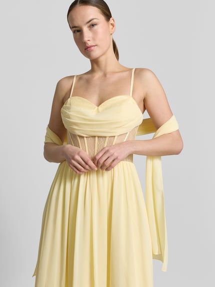 Frauenmodel trägt Corsagenkleid mit Spitze von Mascara in zartgelbem Chiffon, taillierter Schnitt, Spitze, Nahaufnahme Oberkörper.
