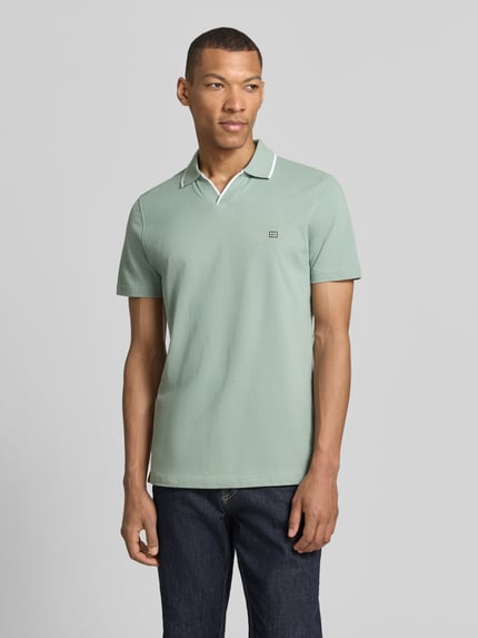 Męski model nosi Modern Fit Poloshirt mit Logo-Stitching von Christian Berg Men z bawełny, kołnierzyk polo, wyhaftowane logo, długość tyłu 71 cm w rozmiarze M, jasna zieleń, gładka faktura, widok całej sylwetki z przodu.