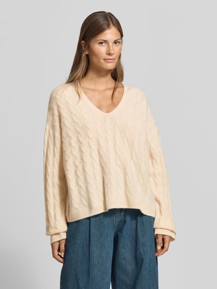Frauenmodel trägt Relaxed Fit Pullover aus reiner Baumwolle von MYON in Creme, Strick-Optik, V-Ausschnitt, Langarm, Ganzkörperansicht von vorne.