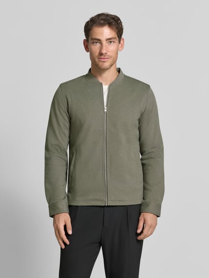 Mężczyzna nosi Slim Fit Sweatjacke mit Stehkragen od Lindbergh, Mieszanka materiałów z dodatkiem streczu, zamek błyskawiczny, wpuszczane kieszenie, krój slim fit, stójka, długość tyłu w rozmiarze M: 67 cm, długość rękawów w rozmiarze M: 66 cm, widok całej sylwetki z przodu.