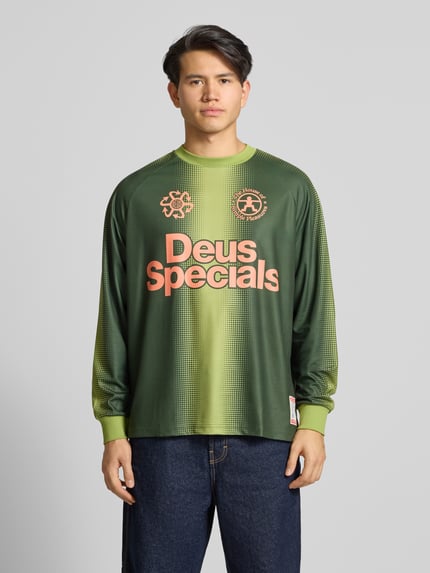 Männermodel trägt Trikot mit Label-Print und Rundhalsausschnitt von DEUS EX MACHINA in Grün, Regular Fit, Longsleeve, Ganzkörperansicht von vorne. Rückenlänge bei Größe M: 71 cm, Ärmellänge bei Größe M: 65 cm.