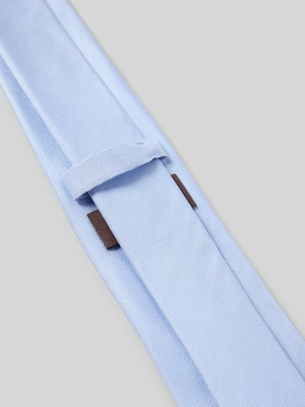 Produktfoto, Krawatte aus reiner Seide von Blick in Hellblau mit Strukturmuster, Teilungsnähte und Label-Detail auf grauem Hintergrund.