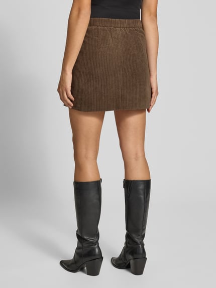 Frauenmodel trägt Ausgestellter Mini-Rock mit seitlichen Reißverschluss Modell 'AUDRE' von PIECES in Braun, gerippte Textur, Ganzkörperansicht Rückansicht. Damen Mini-Rock von PIECES.