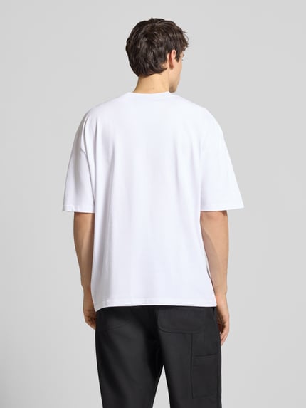 Männermodel trägt Oversized T-Shirt mit Label-Stitching van Pegador, wit katoen, geribde ronde hals, ruglengte 69 cm, Ganzkörperansicht Rückansicht.
