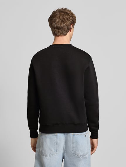 Männermodel trägt Regular Fit Sweatshirt aus Baumwoll-Mix mit Label-Detail von Alpha Industries, schwarze Farbe, Ganzkörperansicht Rückansicht. Herren Sweatshirt, elastische Abschlüsse, Rückenlänge bei Größe M 66 cm.