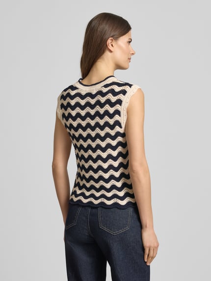 Modelka nosi bezrękawnik 'Pullunder im Allover-Look mit Wellensaum' od Christian Berg Woman, krój regular fit, wzór na całej powierzchni, falisty brzeg, okrągły dekolt, długość tyłu w rozmiarze S: 55 cm, całkowity widok z tyłu.