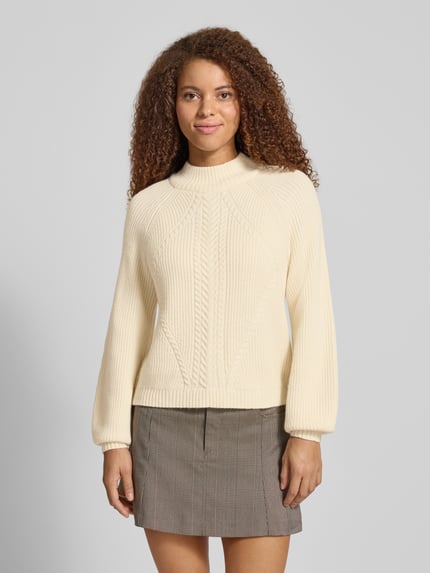 Frauenmodel trägt Regular Fit Strickpullover aus Viskose-Mix Modell 'KATIA' von Only in Creme, Melange-Optik, Zopfmuster, Mock Neck, Raglanärmel, gerippte Abschlüsse, Stricktextur, Ganzkörperansicht von vorne.