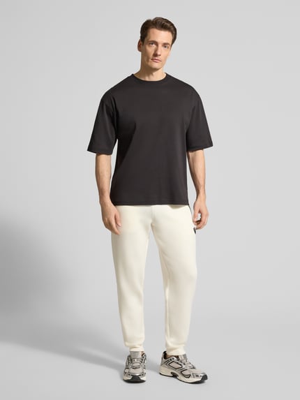 Männermodel trägt Sweatpants mit Viskose-Anteil Modell 'TRAIN PREMIUM SHIELD' von EA7 Emporio Armani in Creme mit geradem Schnitt, Ganzkörperansicht von vorne.