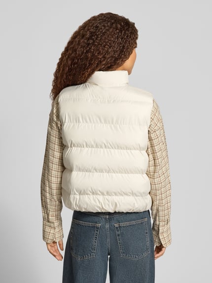 Frauenmodel trägt Steppweste mit Stehkragen Modell 'BOSTON PUFFER VEST' von NEW BALANCE, unifarben, strukturierte Webware, Logo-Print, Reißverschlusstaschen, Ganzkörperansicht Rückansicht.