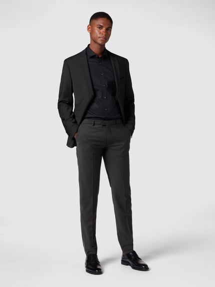 Männermodel trägt Stoffhose mit Bundfalten von Drykorn in Schwarz, Material-Mix mit Baumwoll-Anteil, gerader Schnitt, Ganzkörperansicht von vorne.