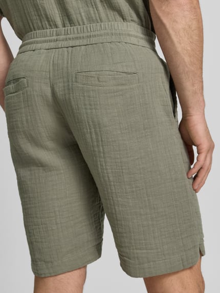 Männermodel trägt Shorts mit Eingrifftaschen und elastischem Bund von Lindbergh in Oliv, Reine Baumwolle, Loose-Fit, Ganzkörperansicht Rückansicht.