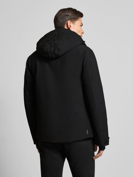 Männermodel trägt schwarze Steppjacke mit Kapuze Modell 'KARRAVAARA' von LUHTA, glatte Struktur, Rückenansicht, Ganzkörperansicht Rückansicht. Regular Fit, Reißverschluss, Reißverschlusstaschen, Ärmelriegel, Maße: Rückenlänge 74 cm, Schulterbreite 47 cm, Brustweite 54 cm, Ärmellänge 66 cm.