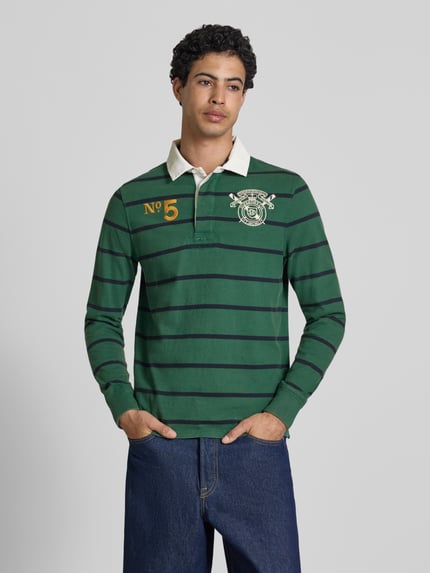 Männermodel trägt Regular Fit Rugby Shirt mit Logo- und Motiv-Stitching von Superdry, grün mit dunklen Streifen, reine Baumwolle, Polokragen, Nahaufnahme Oberkörper.