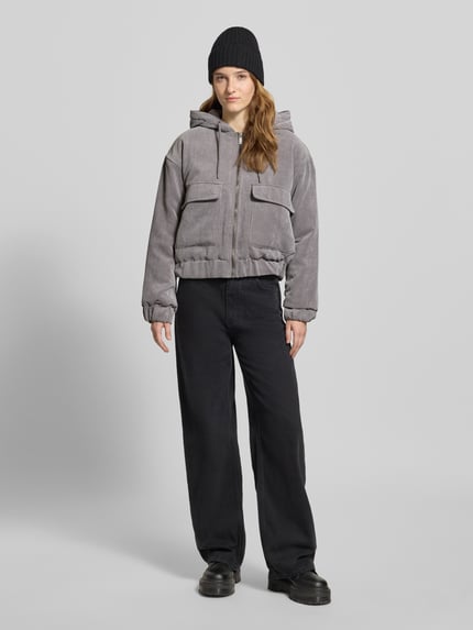 Frauenmodel trägt Regular Fit Bomberjacke mit Kapuze Modell 'SUVA' von Only aus grauem Cord mit gestreifter Struktur, Ganzkörperansicht von vorne.