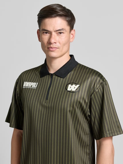 Männermodel trägt Regular Fit Poloshirt mit Label-Print Modell 'Lama' von Wood Wood, Olive mit schwarzen Streifen, Nahaufnahme Oberkörper. Rückenlänge bei Größe M: 72 cm, Polokragen, kurzer Reißverschluss.