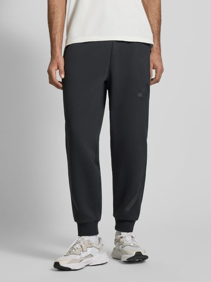 Mannenmodel draagt Sweatpants met Logo en elastische band van adidas Sportswear, materiaalmix met katoen, regular fit, logo, tunnelkoord, binnenbeenlengte maat M 75 cm, voorkant hele lichaam