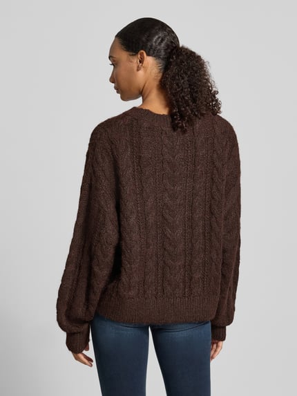 Frauenmodel trägt Oversized Fit Strickpullover mit Zopfmuster von REVIEW in Dunkelbraun, grobe Stricktextur, elastische Abschlüsse, Ganzkörperansicht Rückansicht. Rückenlänge bei Größe S 54 cm, Ärmellänge 58 cm.