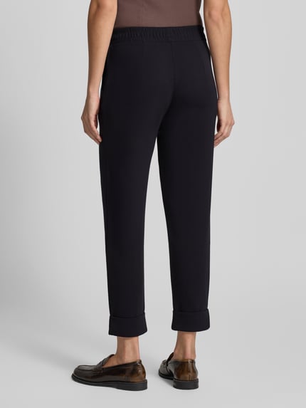Frauenmodel trägt Sweatpants mit elastischem Bund von Christian Berg Woman, Material-Mix mit Modal-Anteil, Regular Fit, Bundfalten, dunkle Farbe, glatte Textur, Ganzkörperansicht Rückansicht.