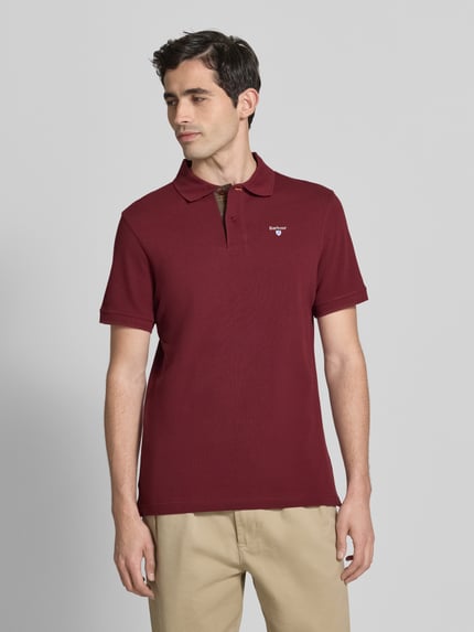 Męski model nosi Regular Fit Poloshirt aus reiner Baumwolle von Barbour, efekt: jednolity kolor, krój regular fit, aplikacja z wyhaftowanym logo, kołnierzyk polo, zapięcie na 2 guziki, krótki rękaw, wykończenie: z rozcięciem, wykończenie materiału: pika, materiał: bawełna, widok całej sylwetki z przodu.