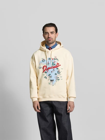 Männermodel trägt Relaxed Fit Hoodie mit Logo-Print von Dsquared2 in Creme, reine Baumwolle, Kapuze mit Tunnelzug, elastische Abschlüsse, Ganzkörperansicht von vorne.