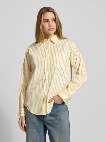 Modelka kobieca nosi Relaxed Fit Bluse mit Brusttasche od Gant, w żółte paski, bawełna, kołnierzyk, kieszeń, guziki, widok całej sylwetki z przodu.