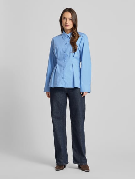 Frauenmodel trägt Hemdbluse aus Baumwoll-Mix Modell 'Zopy' von Gestuz in Blau mit durchgehender Knopfleiste und Sportmanschetten, Ganzkörperansicht von vorne. Taillierte Passform, Hemdblusenkragen, Rückenlänge bei Größe 36: 68 cm, Ärmellänge: 63 cm, glatte Textur.
