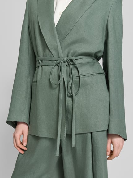 Frauenmodel trägt Anzugblazer mit Reverskragen von Jake*s Collection in Grün, taillierte Passform, Stoffband, Paspeltaschen, Nahaufnahme Oberkörper.