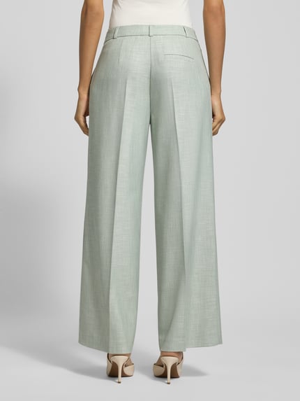 Frauenmodel trägt Wide Fit Stoffhose aus Viskose-Mix mit Bügelfalten von Comma, hellgrün, Gesäßtaschen, Ganzkörperansicht Rückansicht.