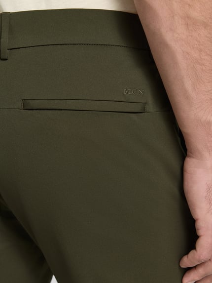 Männermodel trägt Tapered Fit Hose mit Gesäßtaschen von MCNEAL in Olivgrün, glatte Textur, Detailaufnahme Gesäßtasche, Herren HOSE, Eingrifftaschen, Knopf- und Reißverschluss, Bundweite 45 cm, Innenbeinlänge 80 cm, Größe M.