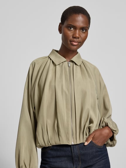 Frauenmodel trägt Jacke aus Lyocell mit Reißverschluss Modell 'Jabana' von OPUS in hellem Olivgrün, Umlegekragen, Relaxed Fit, Nahaufnahme Oberkörper.