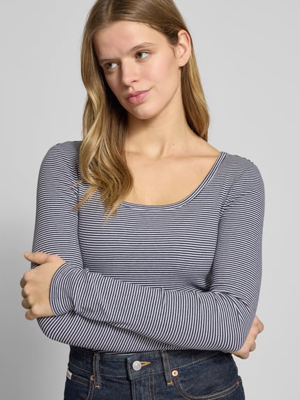 Frauenmodel trägt Slim Fit Longsleeve mit tiefen Rundhalsausschnitt von Review aus elastischem Baumwoll-Mix mit Strukturmuster, Nahaufnahme Oberkörper.