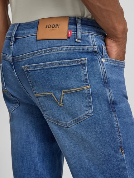 Mężczyznamodel nosi Modern Fit Jeans mit Eingrifftaschen Modell 'Mitch' von JOOP! aus mieszanka bawełny i elastanu, kolor niebieski, tekstura gładka, długość wewnętrzna nogawki 78 cm, szerokość w rozmiarze 32/32: 42 cm, wpuszczane kieszenie, ujęcie z tyłu zbliżenie na kieszeń.