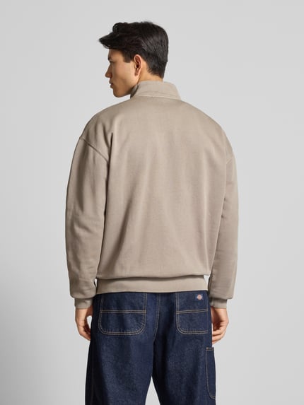 Männermodel trägt Oversized Sweatjacke mit Label-Stitching von Pegador, Baumwoll-Mix, Stehkragen, Reißverschluss, Reißverschlusstaschen, Rückenlänge 70 cm, Ärmellänge 65 cm, beige Farbe, glatte Textur, Ganzkörperansicht Rückansicht.