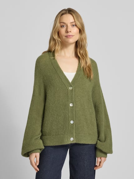 Vrouwenmodel draagt Strickjacke mit V-Ausschnitt Modell 'Petrinelle Hope' van MSCH Copenhagen in olijfgroen, zachte textuur, relaxed fit, knoopsluiting, Ganzkörperansicht van voren.