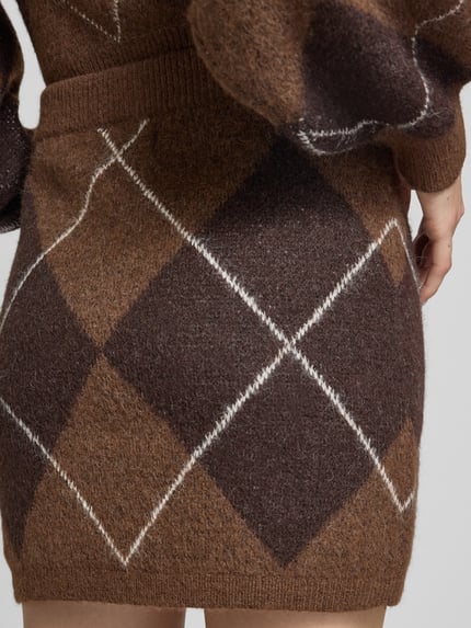 Frauenmodel trägt Minirock mit Argyle-Muster von VERO MODA in Brauntönen, Strickstruktur im Wollmix, Nahaufnahme Hüftbereich.