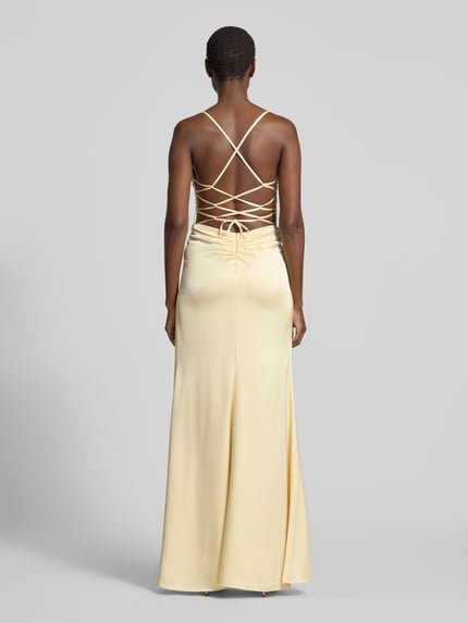Männermodel trägt Abendkleid mit rückseitig überkreuzten Spaghettiträgern von Mascara aus satyna, dopasowany krój, długa sukienka, dekolt w kształcie serca, cienkie ramiączka skrzyżowane z tyłu, wiązanie z tyłu, zapięcie na haftkę i zamek błyskawiczny, długość tyłu w rozmiarze 36: 160 cm, szerokość w rozmiarze 36: 38 cm. Ganzkörperansicht Rückansicht