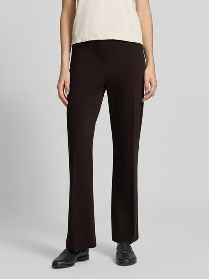 Frauenmodel trägt Schlaghose aus Viskose-Mix mit Bügelfalte von Rich & Royal, dunkle Farbe, elastischer Bund, Nahaufnahme Oberkörper. Damen Stoffhose mit Stretch-Anteil, Bootcut Fit, Bundweite S: 37 cm, Innenbeinlänge S: 73 cm.