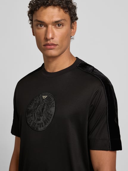 Männermodel trägt T-Shirt mit Label-Detail von Emporio Armani, schwarz, Lyocell-Baumwoll-Mix, Regular-Fit, gerippter Rundhalsausschnitt, Nahaufnahme Oberkörper.